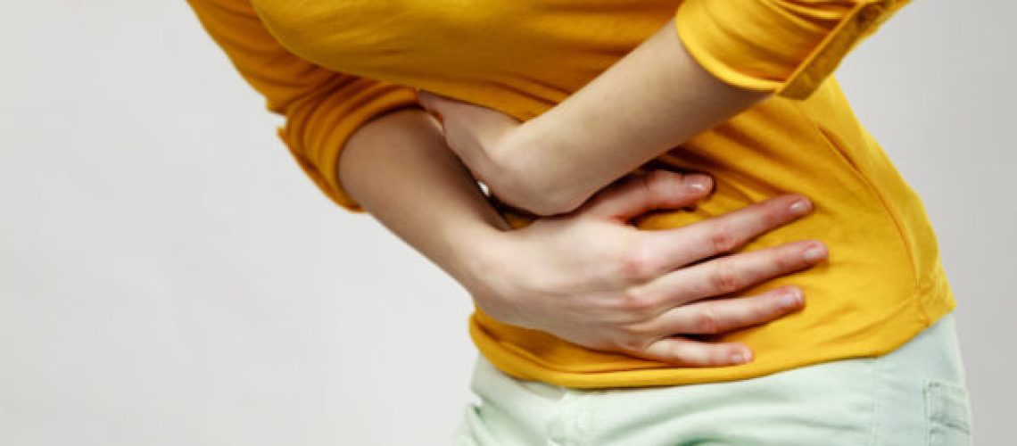 Health care concept. Bellyache, indigestion or menstruation. Young female suffering from strong stomach ache abdominal pain on gray